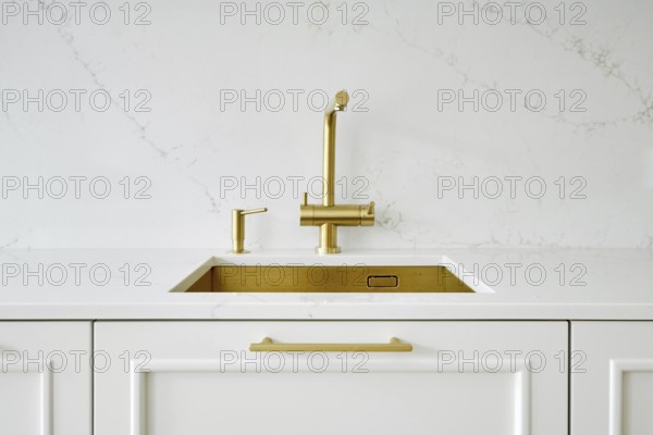 A modern kitchen features a sleek white countertop paired with a gold faucet and sink