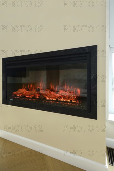 An electric fireplace is set into a wall in a bright living room. Flickering flames illuminate the logs, creating a warm and inviting atmosphere perfect for relaxation