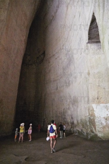 Cave Ear of Dionysus, group of people in a high rock cave, exploring the natural structure, Neapolis Archaeological Park, Syracuse, Sicily, Italy