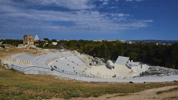 Greek amphitheatre, view of a large ancient amphitheatre with surrounding nature and blue sky with clouds, Neapolis Archaeological Park, Syracuse, Sicily, Italy