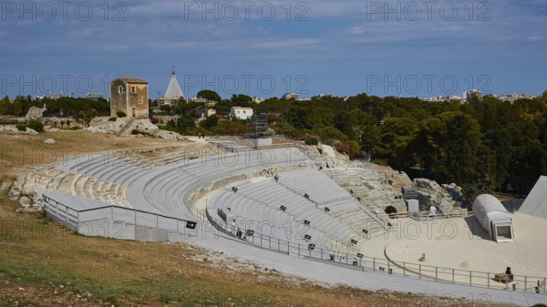 Greek amphitheatre, Ancient amphitheatre surrounded by green trees and historical ruins under a blue sky, Neapolis Archaeological Park, Syracuse, Sicily, Italy
