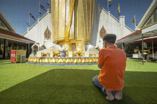 Man praying in front of a 32 metre high standing Buddha decorated with glass mosaics and 24 carat gold, Luang Pho To or Phrasiariyametri, Wat Intharawihan, Bangkok, Thailand