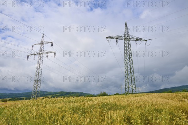 Crop field with electricity pylons, under a cloudy sky, summer, Germerode, Geo nature park Park Frau-Holle-Land, Hoher Meissner, Hesse, Germany