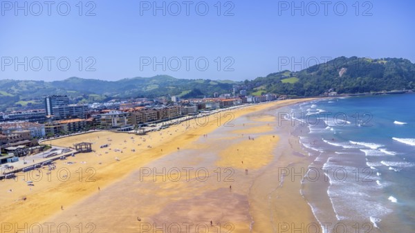Aerial view of zarautz beach during a sunny summer day, featuring golden sand, blue water, and lush green hills in the background, Spain.