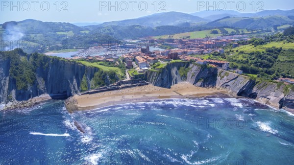 Breathtaking aerial view of zumaia's itzurun beach, cliffs, and cityscape nestled between green hills and the deep blue bay of biscay on a sunny summer day, Spain.