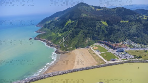Aerial perspective captures the stunning coastal beauty of orio, spain, showcasing the beach, turquoise waters, lush green mountains, and vibrant cityscape.