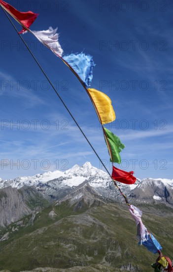 Böses Weibl summit with colourful prayer flags, view of picturesque mountain landscape with snow-covered summit of the Großglockner, Wiener Höhenweg, Schober group, Hohe Tauern National Park, Carinthia, Austria