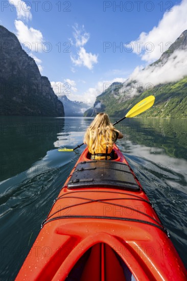Kayak trip on the Geirangerfjord, young woman paddling in a red kayak, atmospheric fjord landscape, Møre og Romsdal, Norway