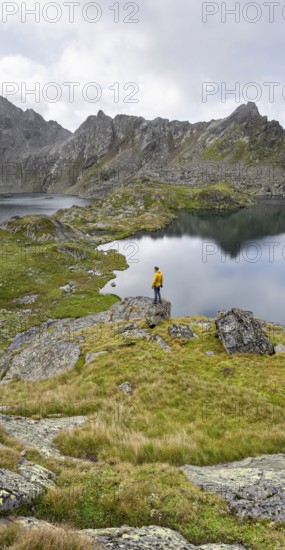 Mountaineer on a rock in front of mountain lakes Wangenitzsee and Kreuzsee, cloudy mountain peaks in the morning, Schober group, Hohe Tauern National Park, Carinthia, Austria