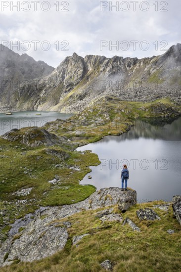 Mountaineer on a rock in front of mountain lakes Wangenitzsee and Kreuzsee, cloudy mountain peaks in the morning, Schober group, Hohe Tauern National Park, Carinthia, Austria