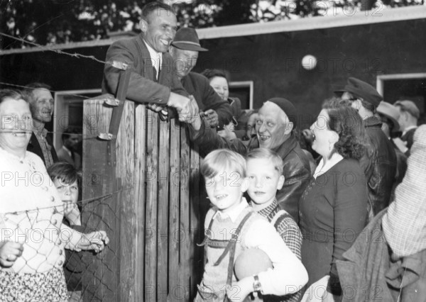 Refugees from the Soviet zone, 1952, A group of people gather around a fence, some smile and shake hands, historical photo