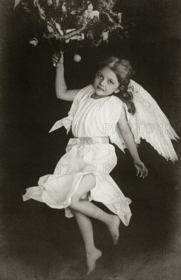 Child angel, 1930s, A child in an angel costume with wings holding a Christmas tree branch, Historical photo