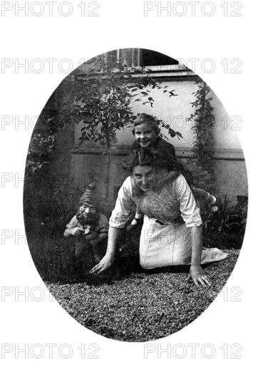 Woman carrying a child on her back, 1920s, A woman crawls on the floor with a child on her back, accompanied by a dwarf figure, Historical photo