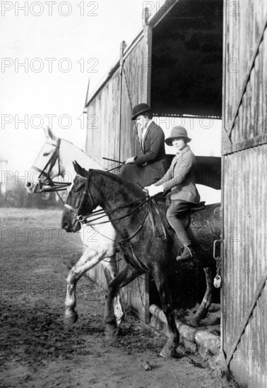 Riding horses out of a barn, 1920s, Two riders on horses coming out of a barn, wearing helmets, Historical photo