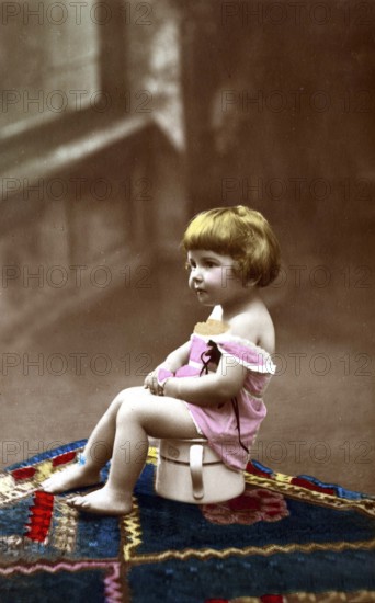 Child sitting on chamber pot, 1920s, A small child sits on a potty, smiles and wears old-fashioned clothes, Historical photo