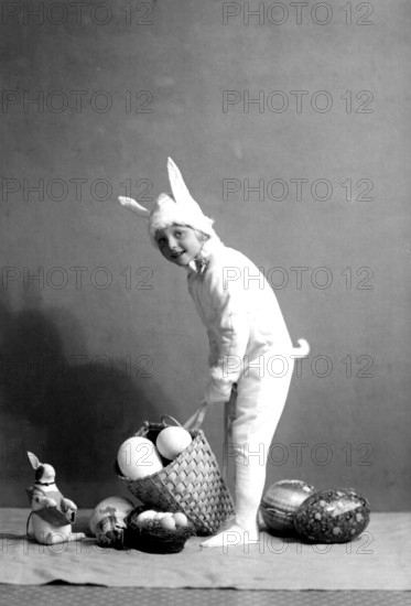 Girl dressed up as an Easter bunny, 1930s, A child in a bunny costume places a basket of eggs on the floor, Historical photo