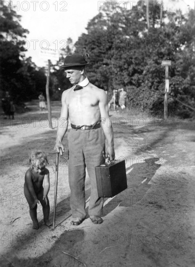 Man with bare upper body travelling with suitcase and son, 1920s, A man with hat and suitcase stands next to a child on a forest path, Historical photo