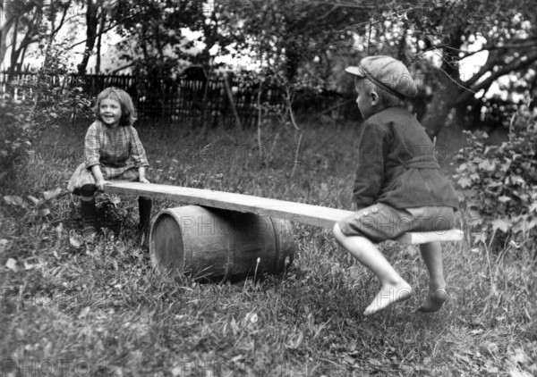 Two children swinging in the garden, 1930s, Two children playing happily on an improvised seesaw in a garden, Historical photo
