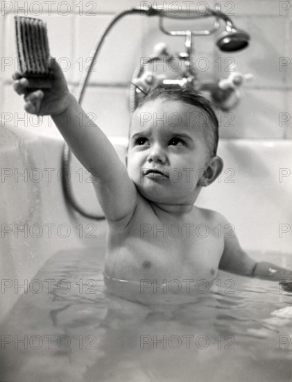 Little boy playing with a wooden car, 1930s, Baby in the bathtub holding up a toy and looking sideways with concentration, historical photo