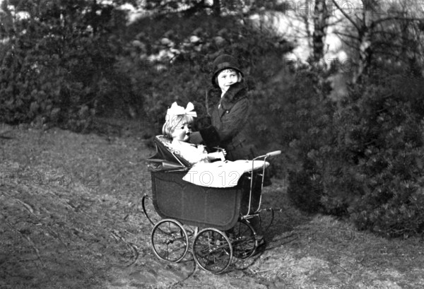 Girl playing with doll, 1920s, Woman with hat and fur collar pushing an antique pram in the forest, Historical photo