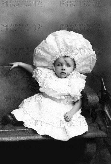 Girl on a bench, 1920s, Child with big hat in vintage clothes sitting on a bench, Historical photo