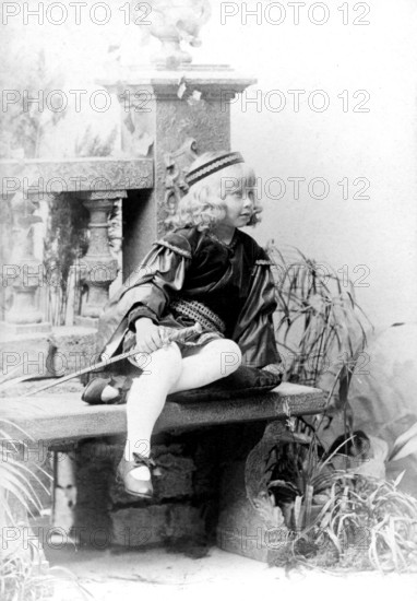 Dressed up girl with sword, 1930s, child in costume sitting on a stone bench, black and white scene with decorative elements, historical photo