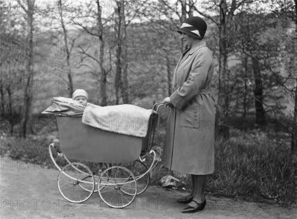 Woman pushing pram, 1920s, Woman with hat standing next to a pram and laughing with the baby lying in it, historical photo