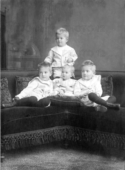 Small children sitting on sofa, 1930s, Four children in classic clothes sitting together on a couch and looking seriously into the camera, Historical photo