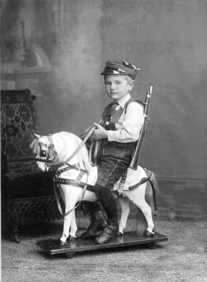 Little boy sitting on a rocking horse, 1910s, Boy in traditional clothing riding a wooden rocking horse and looking confidently into the camera, Historical photo