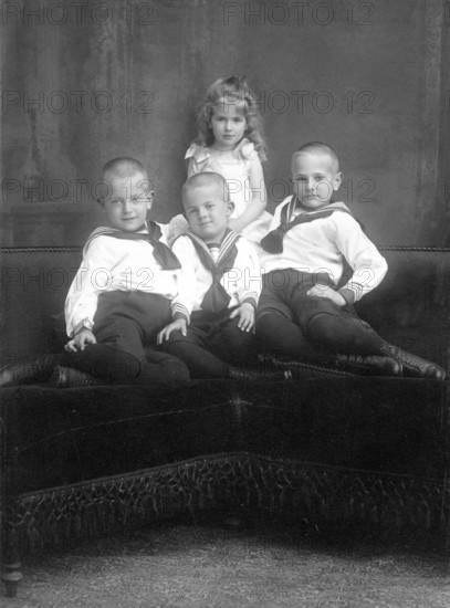 Three boys and a girl, 1930s, Three boys and a girl in traditional dress pose together on a sofa, Historical photo