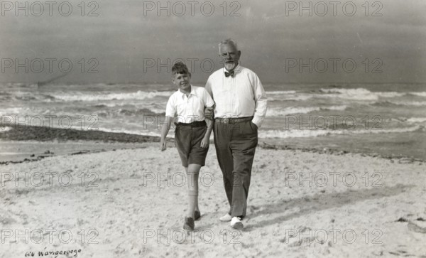 Grandpa and grandson on the beach of Wangerooge, 1930s, Elderly man and boy walking along the beach, the sea in the background, Historical photo
