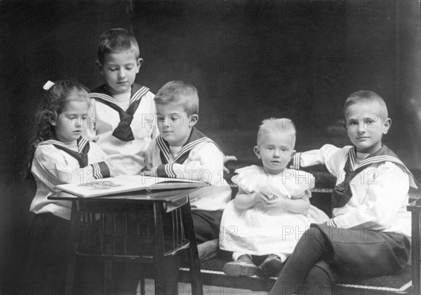 Group photo of small children, 1930s, Five children in sailor suits reading a book together and showing concentrated interest, Historical photo