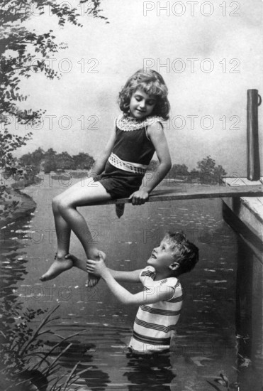 Boy holding girl by the foot, 1920, A boy happily lifting a girl, both in swimwear enjoying the summer on the river bank, Historical photo