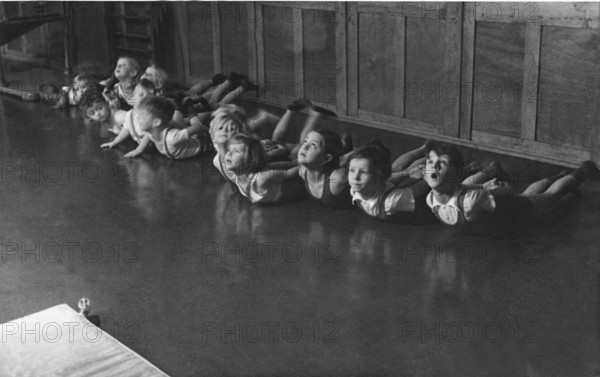 Group of children doing gymnastics, 1930s, children doing floor exercises in a row on the floor, historical photo