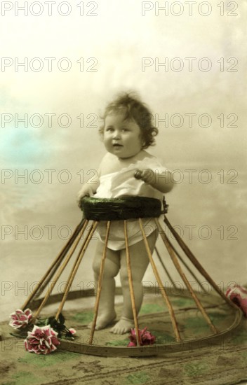 Baby in a frame, walking aid, 1910s, A baby stands in a tyre with flowers, in retro style, Historical photo