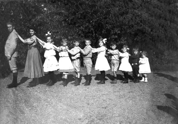 Large family posing in size, organ pipes, 1920s, children in a row, holding each other by the shoulders. Historical clothing and cheerful atmosphere outdoors, historical photo