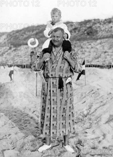 Man in bathrobe carrying child on shoulders, 1930s, A father carries his child on his shoulders on a sandy beach, Historical photo