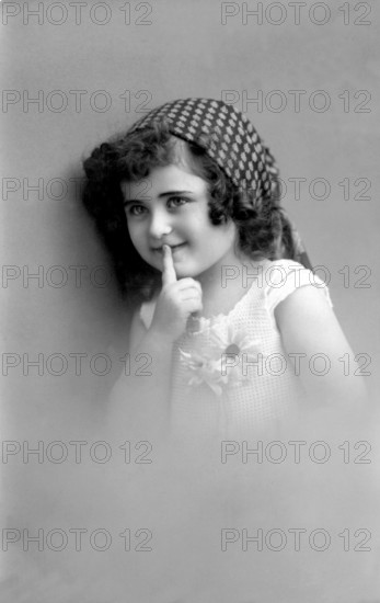 Girl is quiet, 1920s, Young girl with headscarf puts finger on lips and smiles mischievously, Historical photo