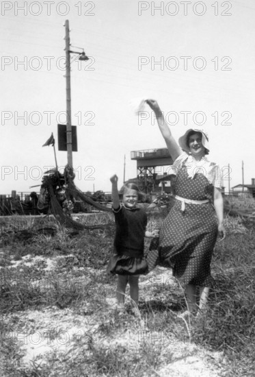 Woman and child saying goodbye, 1930s, Woman and child raising their hands in the air in greeting, standing on a grassy area, Historical photo