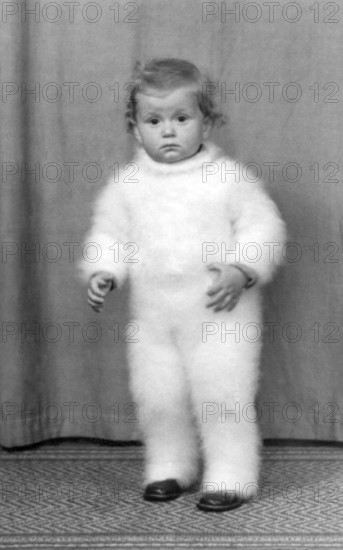 Toddler with funny romper suit, 1930s, Toddler in a fluffy suit, standing on a carpet, looking seriously into the camera, Historical photo