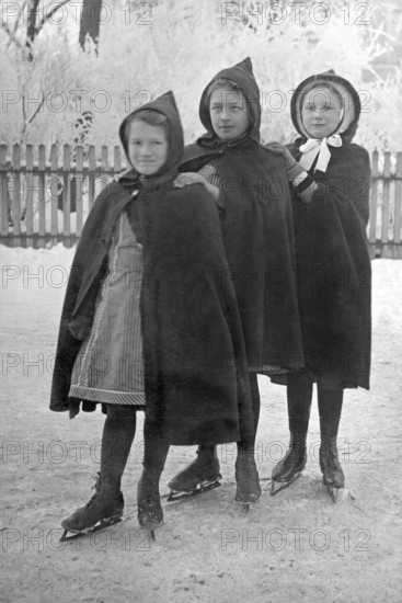 Three girls skating, 1930s, Three girls in hooded coats standing close to each other on an ice rink, Historical photo