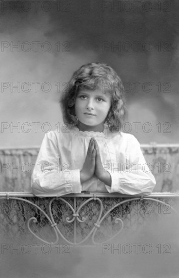 Girl praying at bedside, 1930s, A girl prays with folded hands in front of a bed, Historical photo