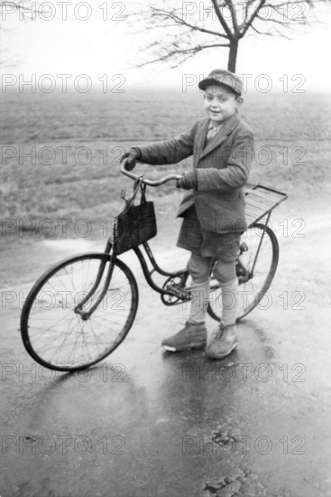 Boy with bicycle, 1920s, Boy standing with bicycle on a wet road in a rural environment, Historical photo
