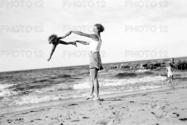 Woman with child on the beach, 1920s, Woman playfully turning a child on the beach while the sea can be seen in the background, historical photo