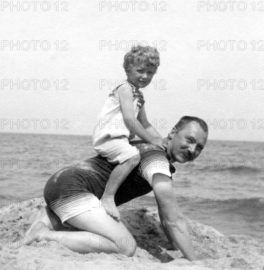 Son sitting on his father on the beach, 1920s, A man on his hands and knees with a happy child on his back on the beach, Historical photo