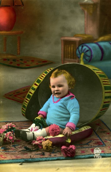 Child sitting in hatbox, 1905, A child sits in a half-opened, large Easter egg prop with flowers, historical photo