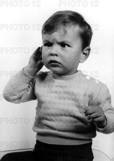 Annoyed child, 1950s, A little boy in a jumper with a questioning expression holds his hand to his ear, Historical photo