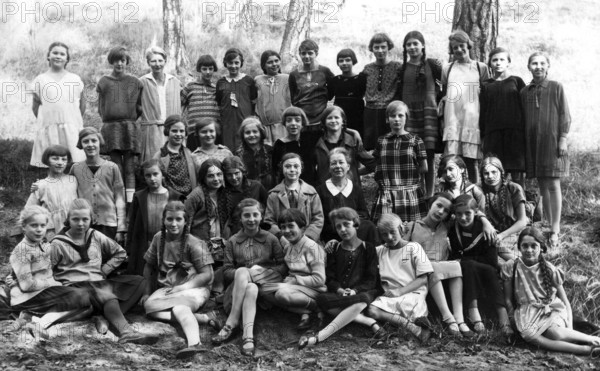 Girls class outing, 1930s, Large group of girls in school uniforms sitting outside in a wooded area, Historical photo