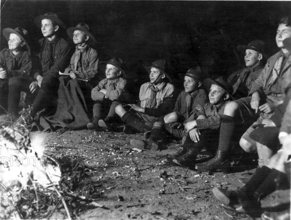 Scout campfire, 1930s, Group of boys in scout suits sitting attentively around a campfire in the dark, historical photo
