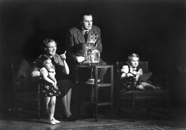 Family home cinema, 1930s, A family sits together in front of a film projector and watches with excitement, historical photo